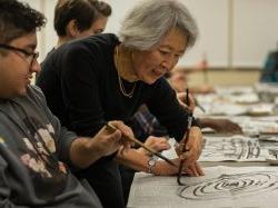 Professor in Calligraphy class drawing spiral on newspaper in front of student at the College of Humanities and Social Sciences